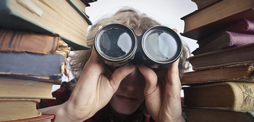 photo of person looking through binoculars between two stacks of books