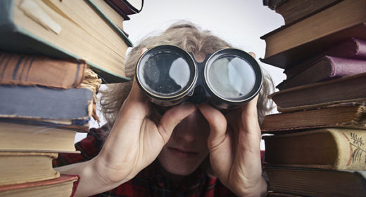 photo of person looking through binoculars between two stacks of books